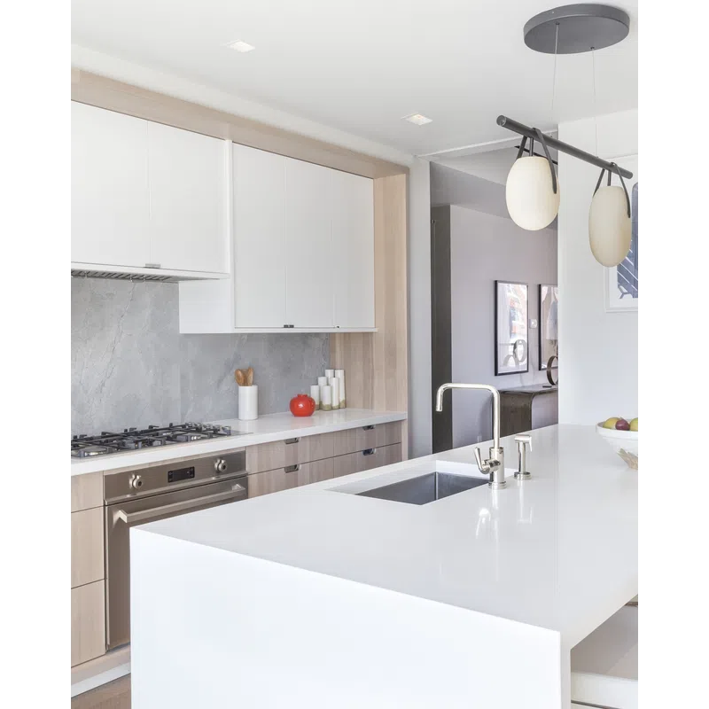 Modern kitchen with white island, stainless steel sink and stove, light wood cabinetry, and contemporary lighting.