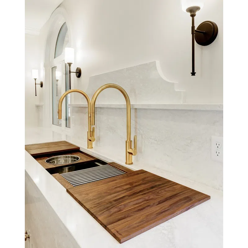 Modern kitchen sink area with dual gold faucets, marble countertops, wooden cutting boards, and wall sconces.