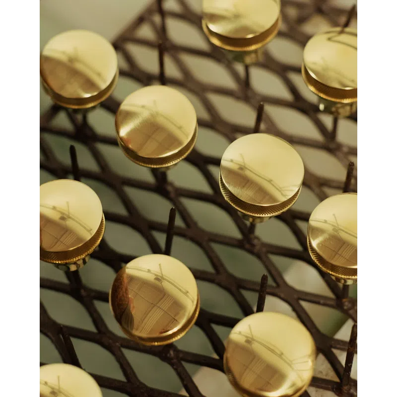 Close-up of shiny gold circular knobs arranged on a metal grid surface with reflections visible on each knob.