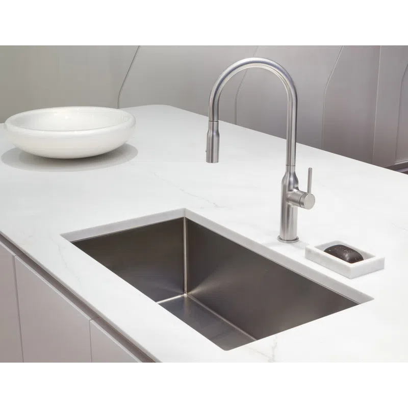 Modern kitchen sink with stainless steel faucet and white marble countertop featuring a soap dish and bowl.