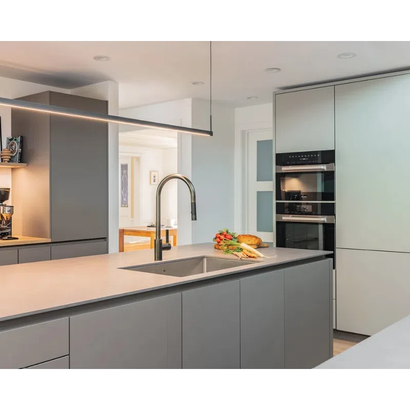 Modern kitchen with gray cabinetry, built-in ovens, a large island with sink, and fresh vegetables on countertop.