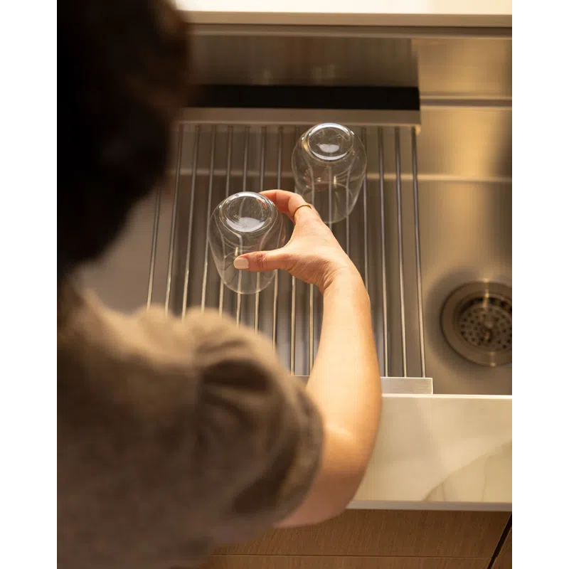 Person placing inverted glass on drying rack beside stainless steel kitchen sink under warm light.