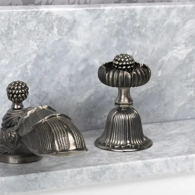 Ornate silver decorative objects with ribbed and fruit-inspired designs on a marble surface.