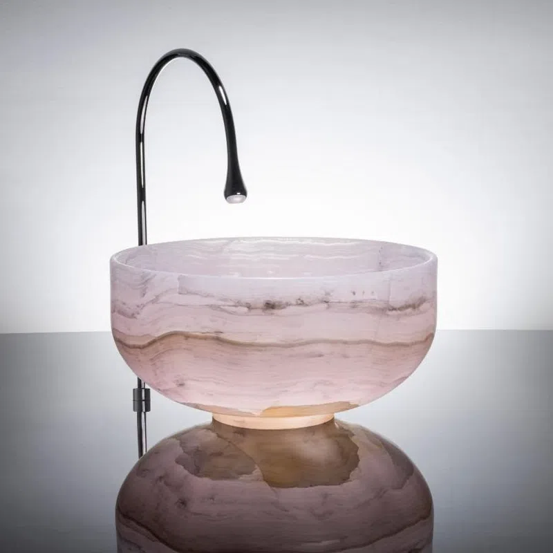 Modern bathroom sink with a polished metal faucet and round marble basin on reflective surface.