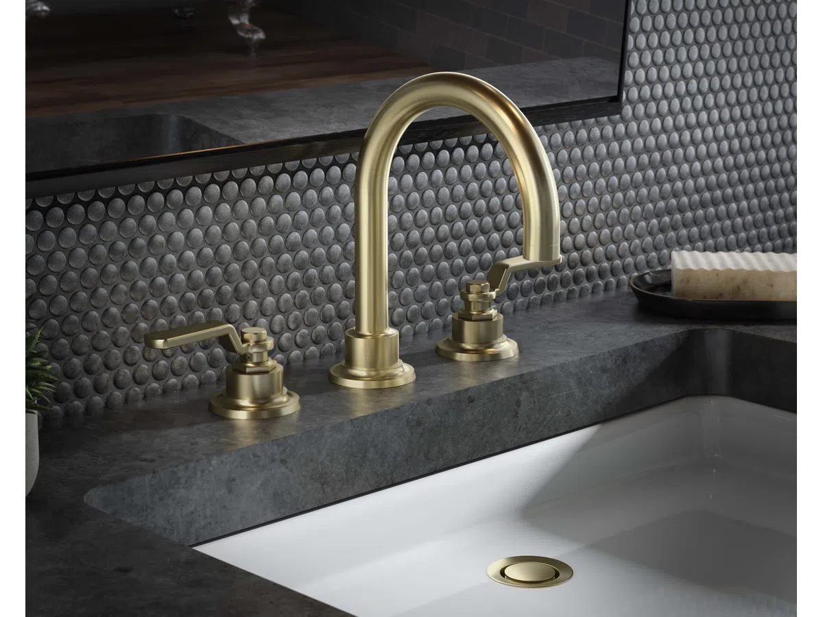 Modern bathroom sink with brushed gold faucet and gray penny tile backsplash under a mirror.