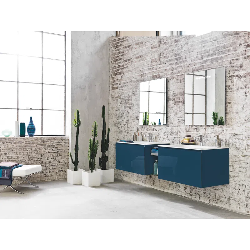 Modern bathroom with blue floating vanity cabinets, white brick walls, tall cacti, and large industrial-style windows.