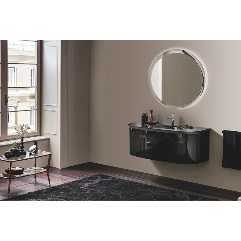 Modern bathroom with a floating black vanity, round backlit mirror, wooden floor, and a window with white shutters.