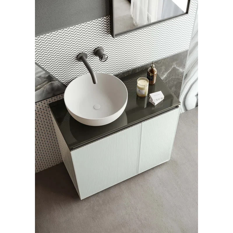 Modern white bathroom sink with round basin, black countertop, patterned wall, and vanity cabinet below.