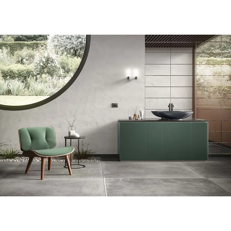 Modern bathroom interior with green vanity, round window overlooking garden, green chair, and gray floor tiles