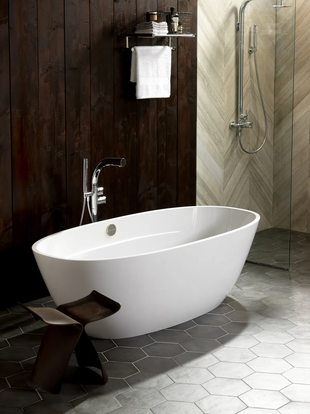 Modern bathroom with white freestanding bathtub, dark wood wall, hexagon floor tiles, and glass shower.