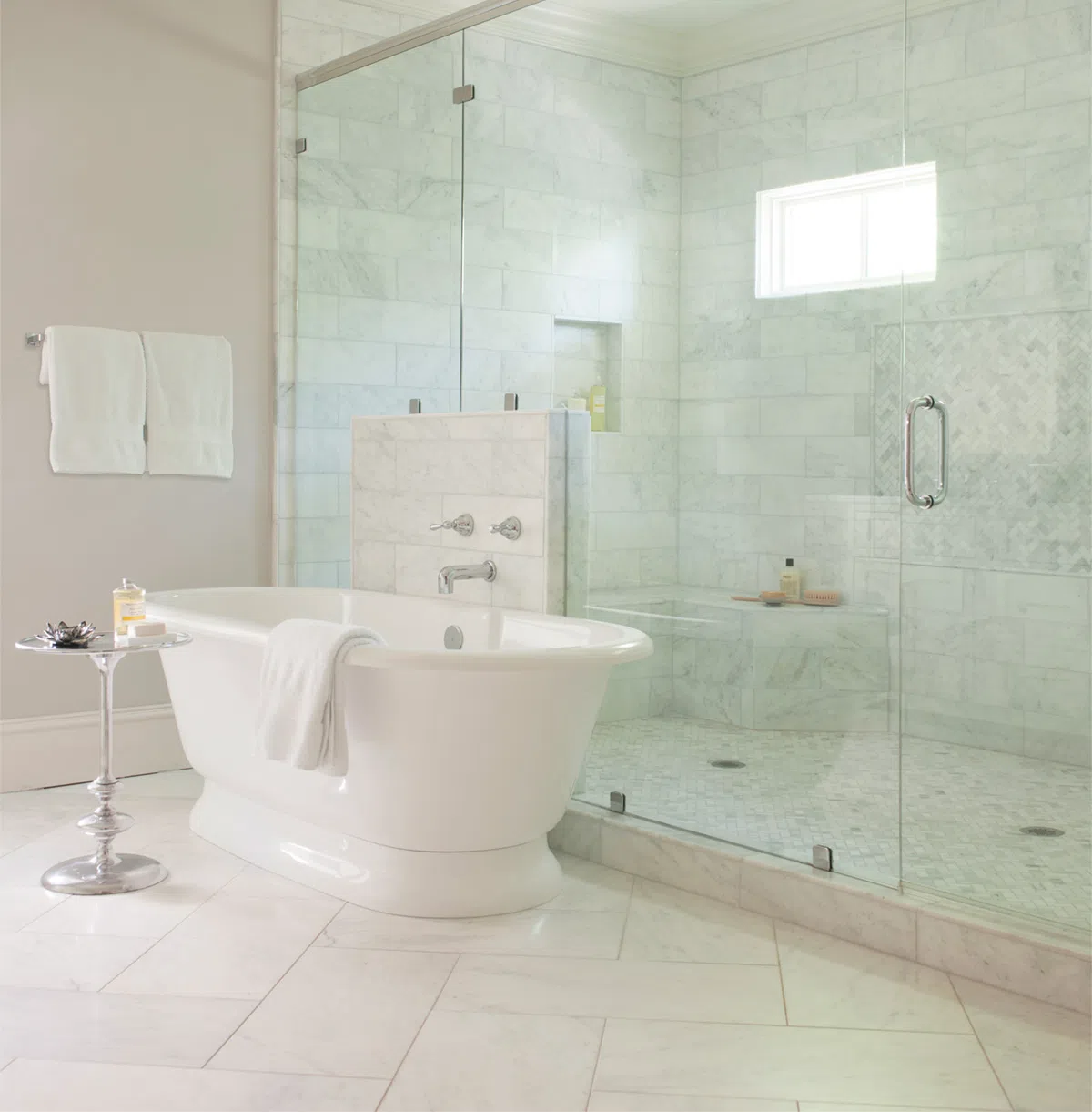 Modern bathroom with white freestanding tub, glass shower enclosure, marble tiles, and chrome fixtures.