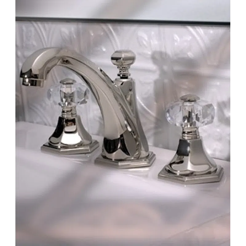Polished chrome bathroom faucet with crystal clear dual handles on a white sink with embossed tile backsplash.