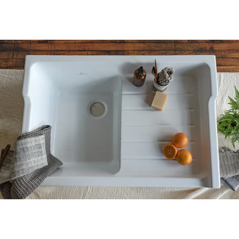 White kitchen sink with oranges, soap bottle, cleaning brush, and folded towels on wooden table.