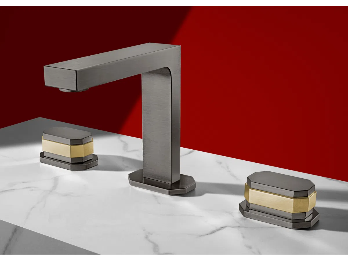 Modern metallic faucet and dual handles with gold accents on white marble countertop against red wall.