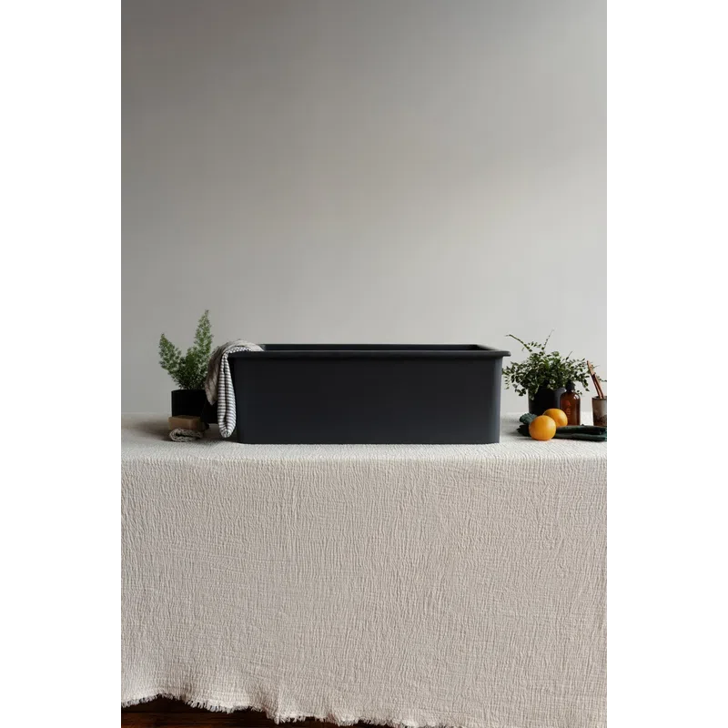 Black rectangular storage bin on textured cream tablecloth with plants, oranges, and bathroom items around it