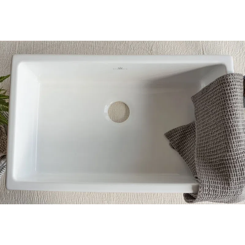 Empty rectangular white ceramic sink with central drain hole and gray textured towel on the right side.
