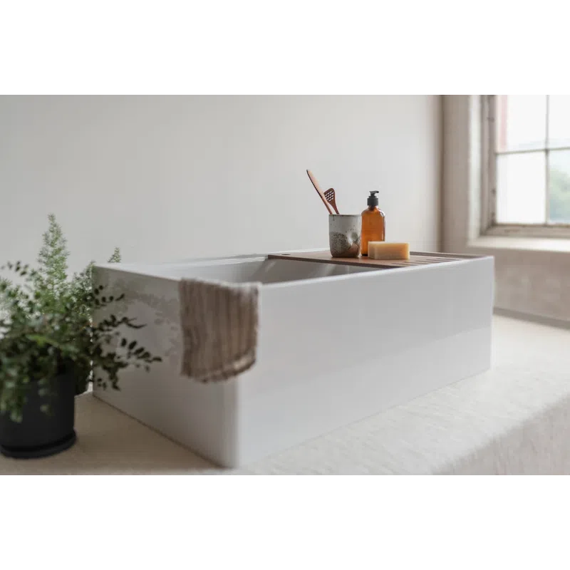 Modern white bathtub with bath accessories and a towel in a bright, minimalist bathroom with a potted plant.