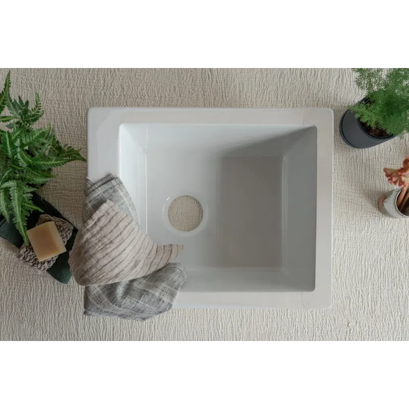 Top view of a clean white rectangular sink with a hole for drainage surrounded by plants and towels.