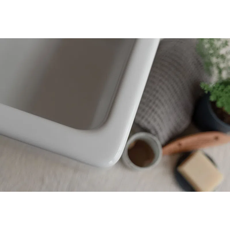 Close-up of a white ceramic sink corner with bath accessories and towel in soft focus.