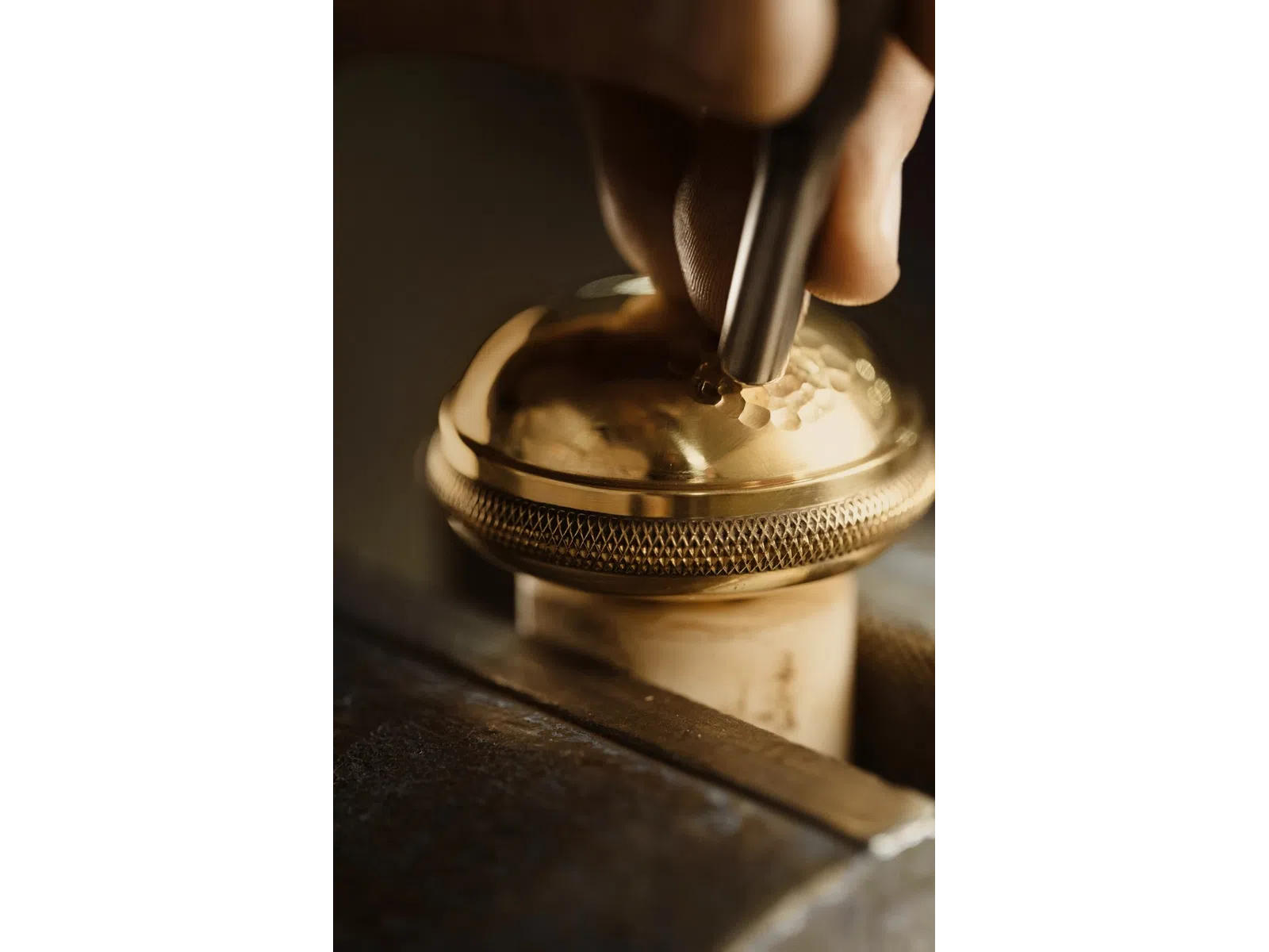Close-up of hand engraving intricate patterns onto a shiny golden metal surface with engraving tool.