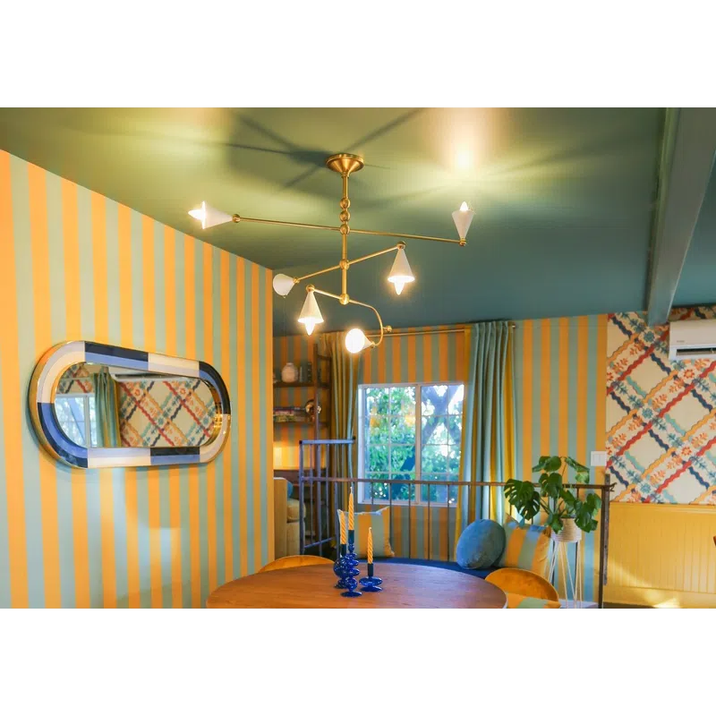 Cozy dining area with round wooden table, mustard yellow chairs, striped walls, and modern chandelier.
