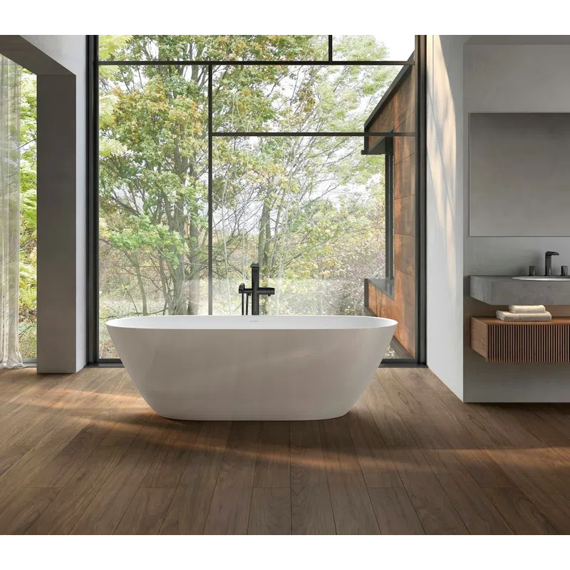 Modern bathroom with freestanding white tub, large floor-to-ceiling window overlooking leafy green trees, wooden floor