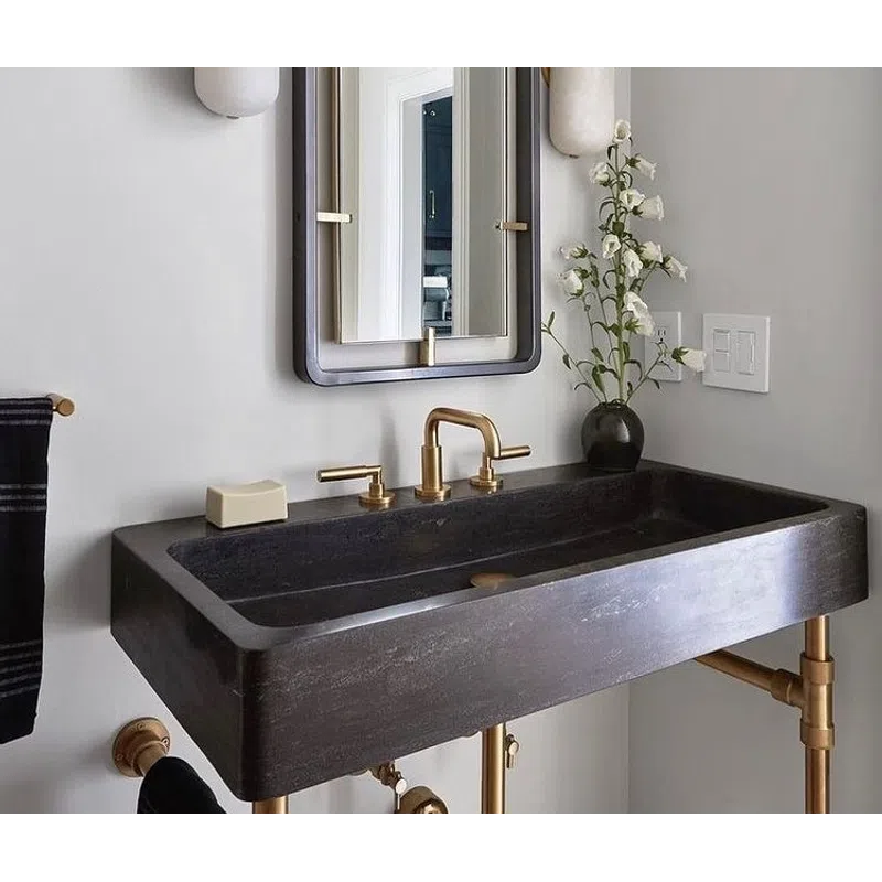 Modern bathroom with a black rectangular sink, brass faucet, wall sconces, mirror, and floral decor on a white wall.