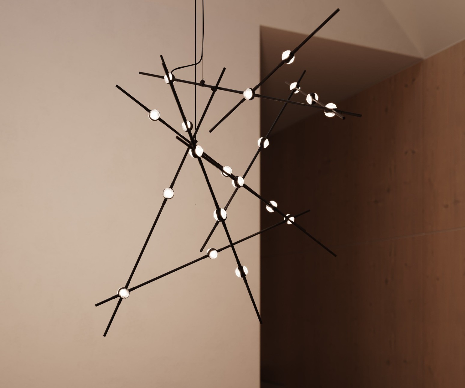 Modern black geometric chandelier with round lights hanging above a wooden table in a minimalist room.