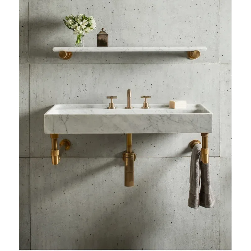 Modern marble sink with brass fixtures and a towel, concrete wall and floating marble shelf with flowers and container.