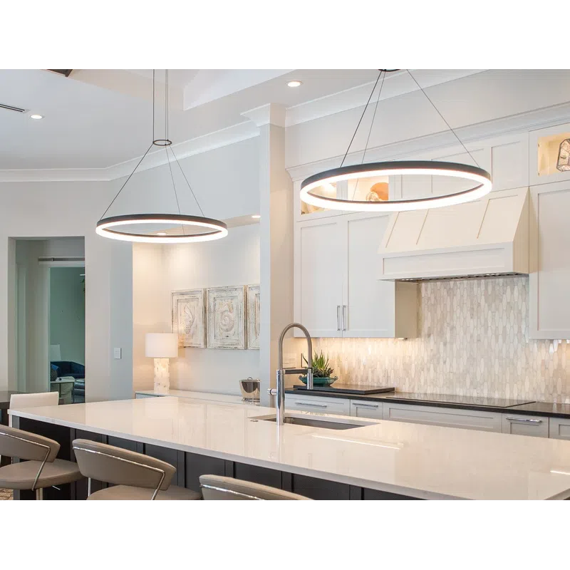 Modern kitchen with a large white island, beige bar stools, circular pendant lights, and white cabinetry.