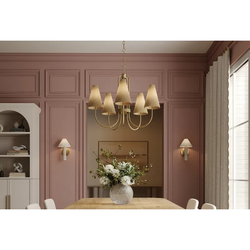 Modern dining room with wooden table, upholstered chairs, pink walls, abstract rug, and gold chandelier lighting.