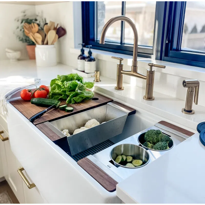 Modern kitchen sink with brass faucet, fresh vegetables on wooden cutting board, and stainless steel prep bowls.