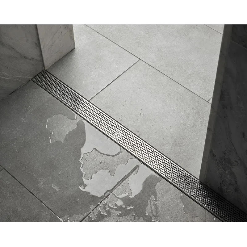 Modern bathroom floor with large gray tiles, wet area, and linear metal drainage grate beside marble walls.