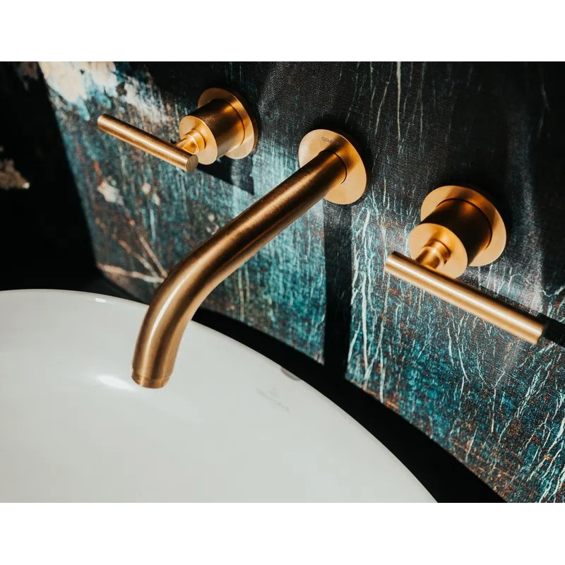 Modern bathroom faucet with brushed gold handles mounted on a dark textured wall above a white sink.
