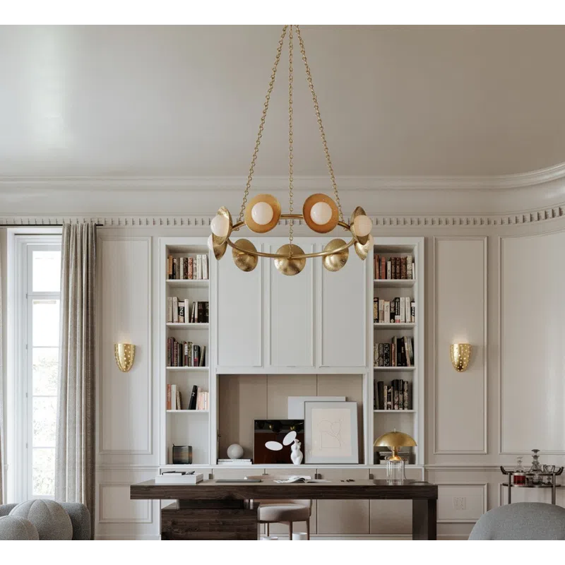 Modern living room with curved gray sofas, round stone coffee table, dark wood desk, and brass chandelier.