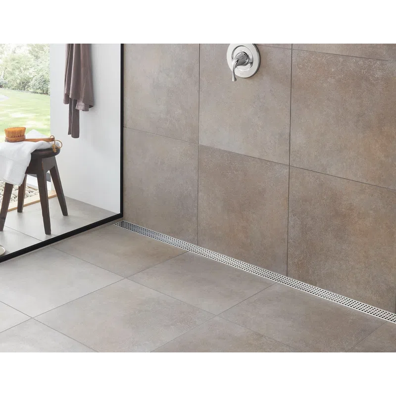 Modern bathroom shower area with large grey tiles, a wooden stool, plants, and a glass partition.