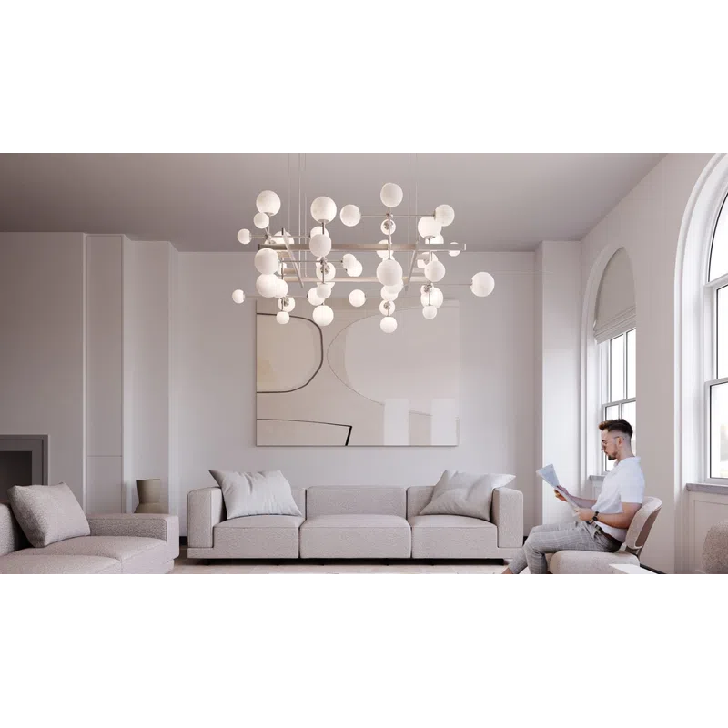Modern minimalist living room with neutral sofas, abstract art, large chandelier, and man reading by arched windows.