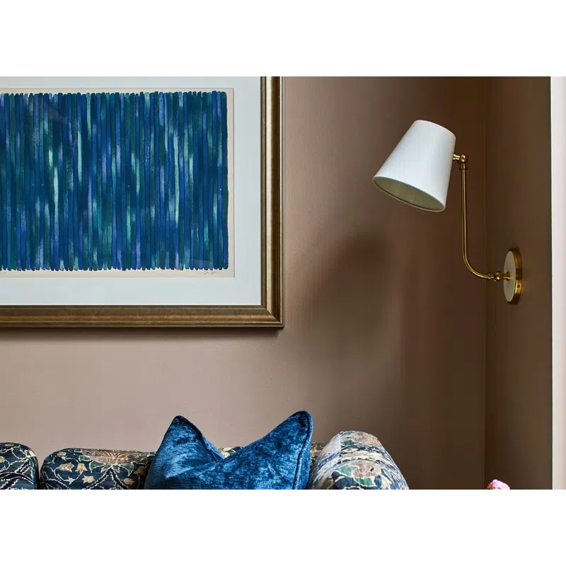 Cozy corner with floral patterned sofa, plush blue pillow, marble side table with vase, and modern wall lamp.