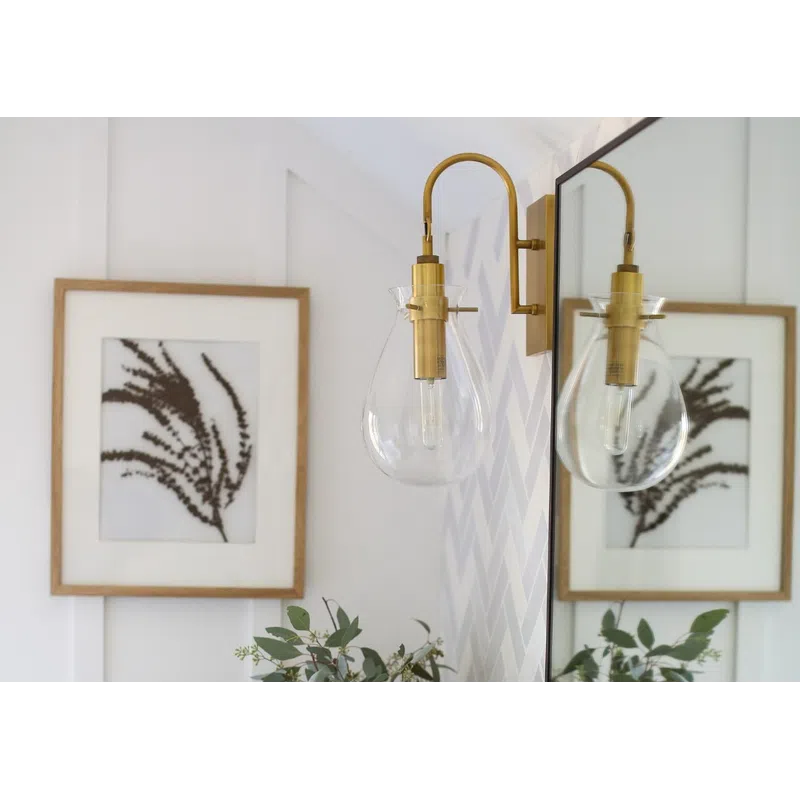 Modern bathroom counter with marble top, potted green plant, candle, brass wall light, and framed botanical print.