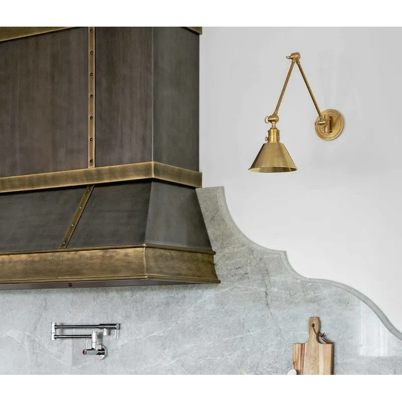 Modern kitchen with brass range hood, marble backsplash, gas stove with red knobs, and wooden utensils.