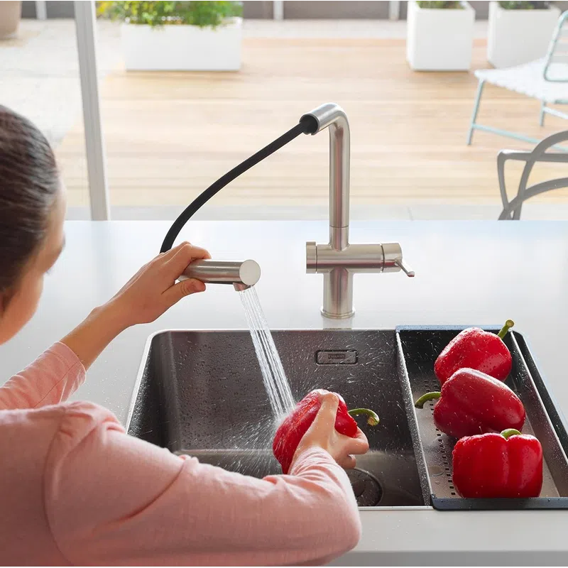 Person washing red bell peppers under a modern kitchen faucet over a black sink with natural light.