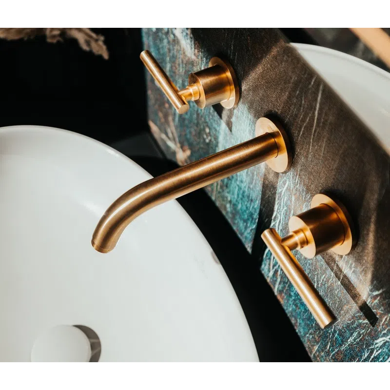 Modern bathroom sink with white basin and gold faucet handles mounted on dark textured wall.