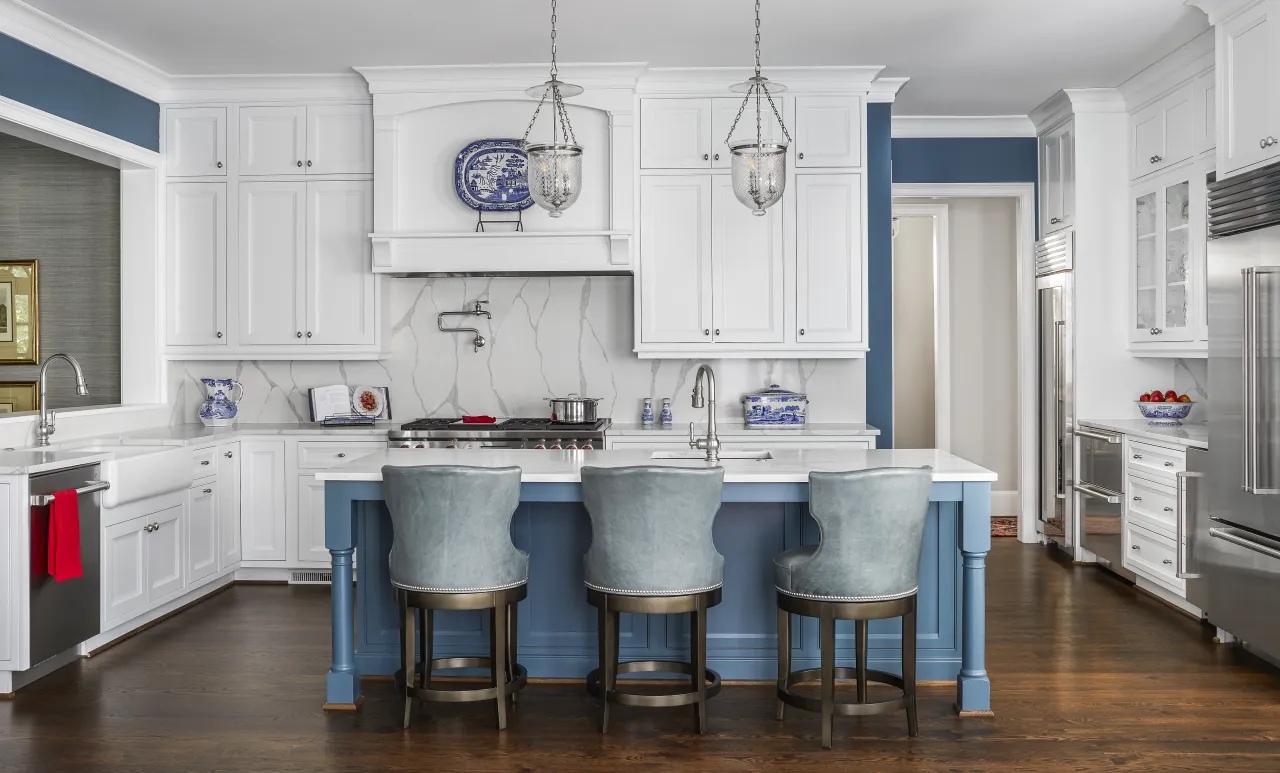 Modern white kitchen with blue island, three gray bar stools, marble backsplash, and stainless steel appliances.