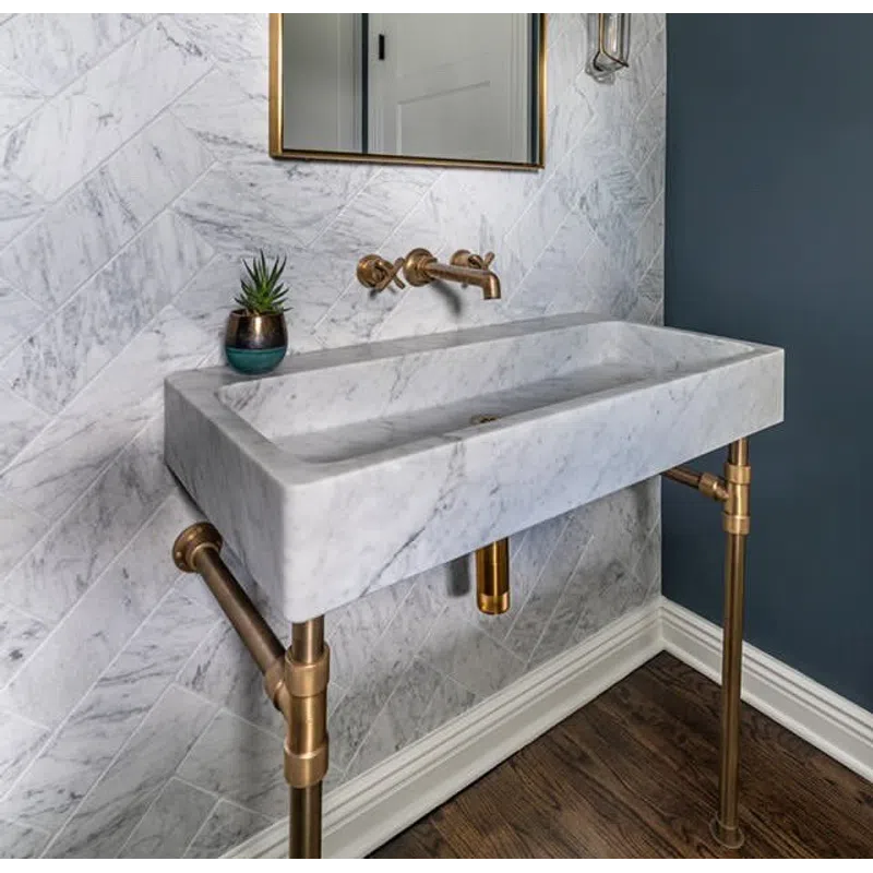 Modern bathroom with marble sink, brass fixtures, chevron marble wall tiles, and a blue accent wall.