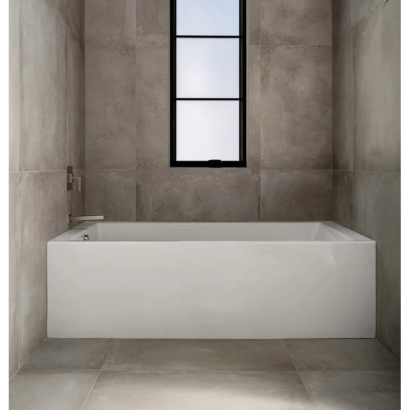Minimalist bathroom with a modern rectangular white bathtub, grey tiled walls, and a tall frosted window.