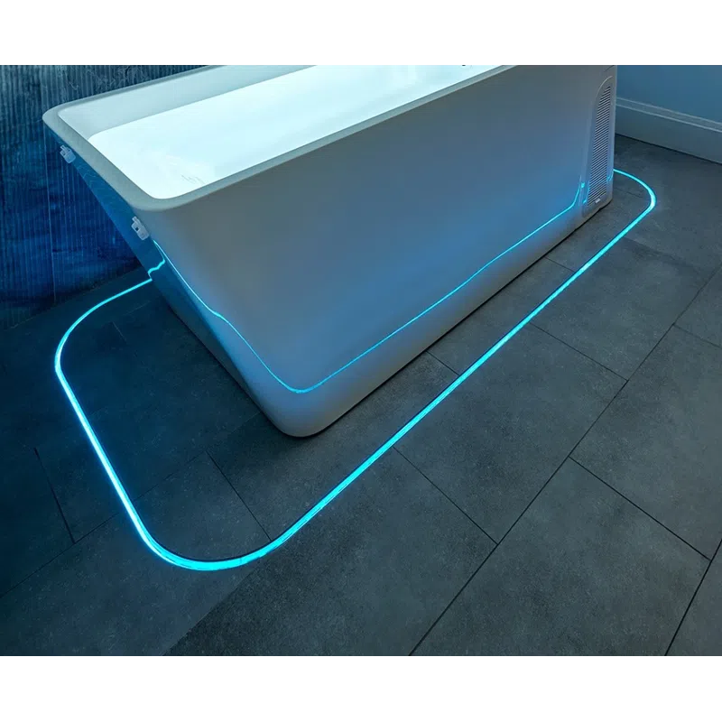 Modern white bathtub with blue LED lighting on gray tiled floor and marble wall background in bathroom