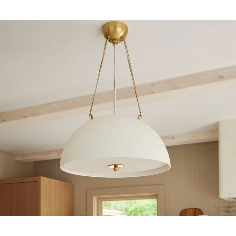 Modern kitchen with white dome pendant light, wooden cabinets, brass fixtures, and a window overlooking greenery.