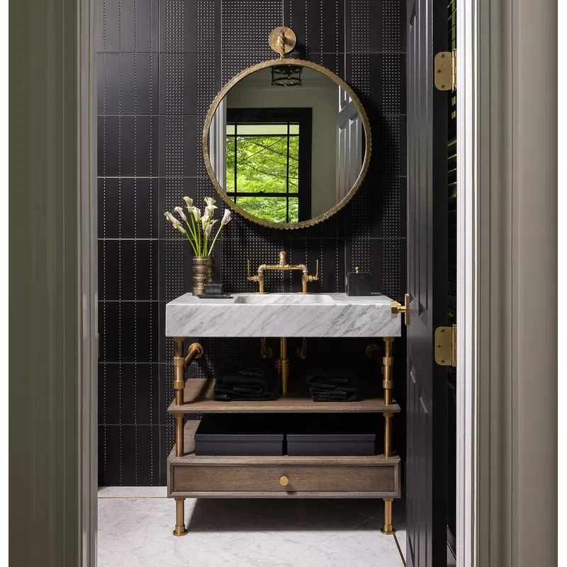 Modern bathroom with marble sink, gold fixtures, round mirror, and black tiled wall with decorative patterns.