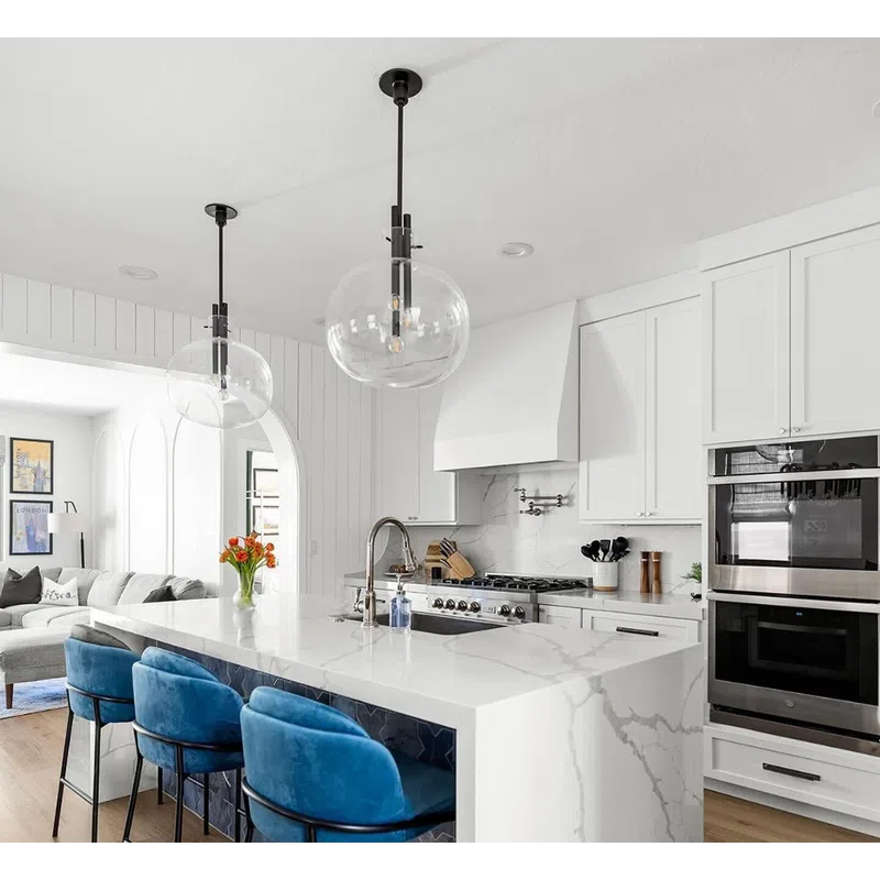 Modern white kitchen with marble island, blue velvet bar stools, pendant lights, and stainless steel appliances