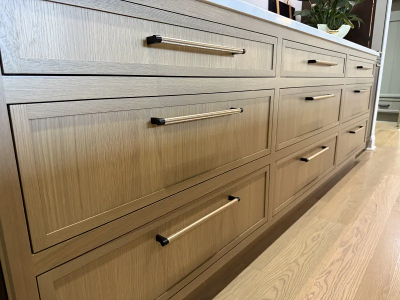 Close-up of modern light wood kitchen cabinets with sleek horizontal metal handles and hardwood floor.